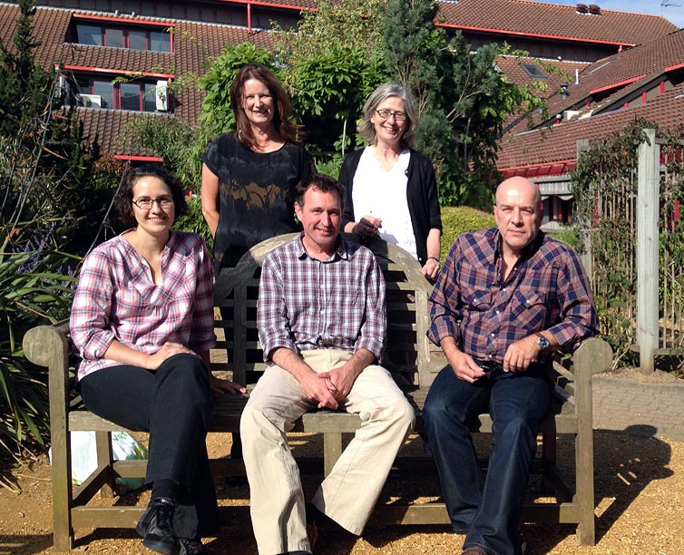 Photo of five project members, three sitting on a bench and two standing behind, in the grounds of MoDiP in Bournemouth